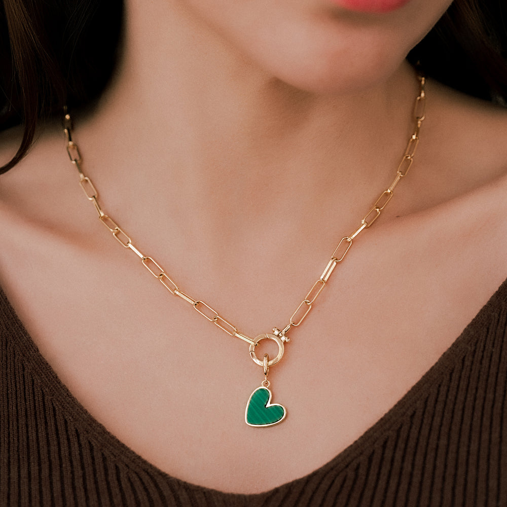 Gold chain necklace with a green heart pendant worn by a person.