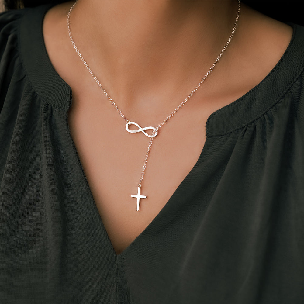 Silver necklace with infinity and cross pendants on a person wearing a black top.