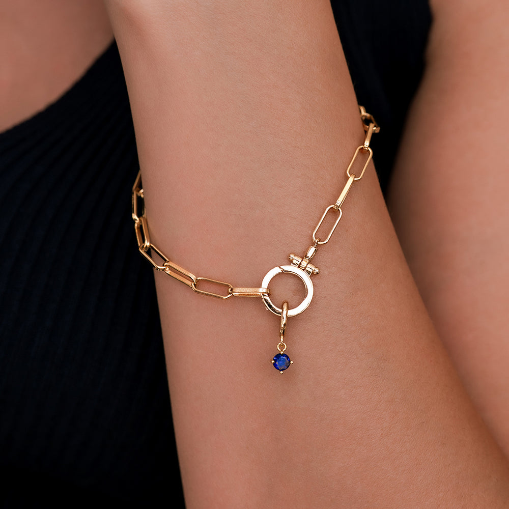 Gold bracelet with a blue gemstone on a wrist against a black background