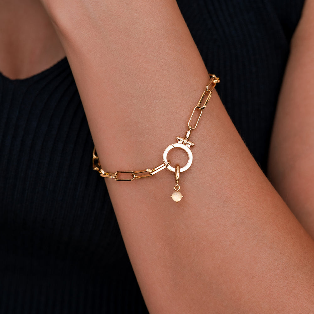 Gold bracelet with a circular charm on a wrist against a black background