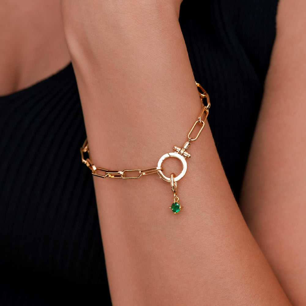 Gold bracelet with a green gemstone on a wrist against a black background