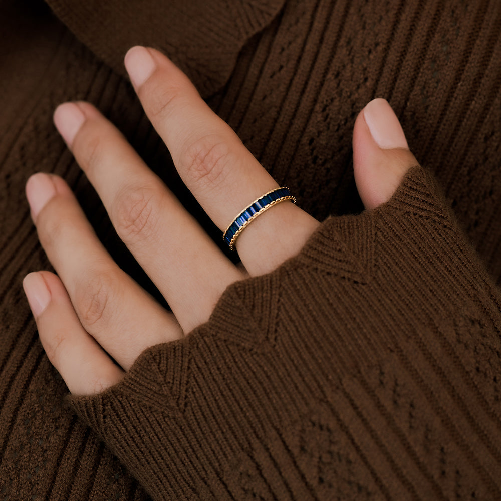 Hand wearing a blue ring with gold accents against a brown textured background
