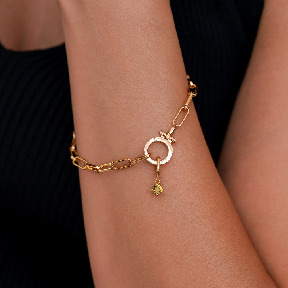 Gold bracelet with a green gemstone on a wrist against a black background