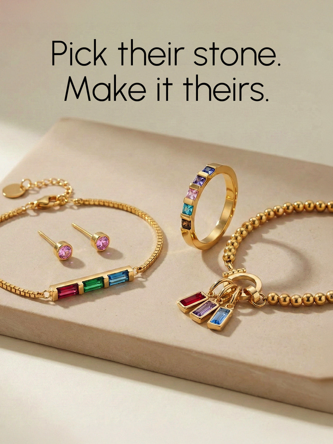 Gold jewelry set with gemstones on a beige surface, including a necklace, bracelet, ring, and earrings.