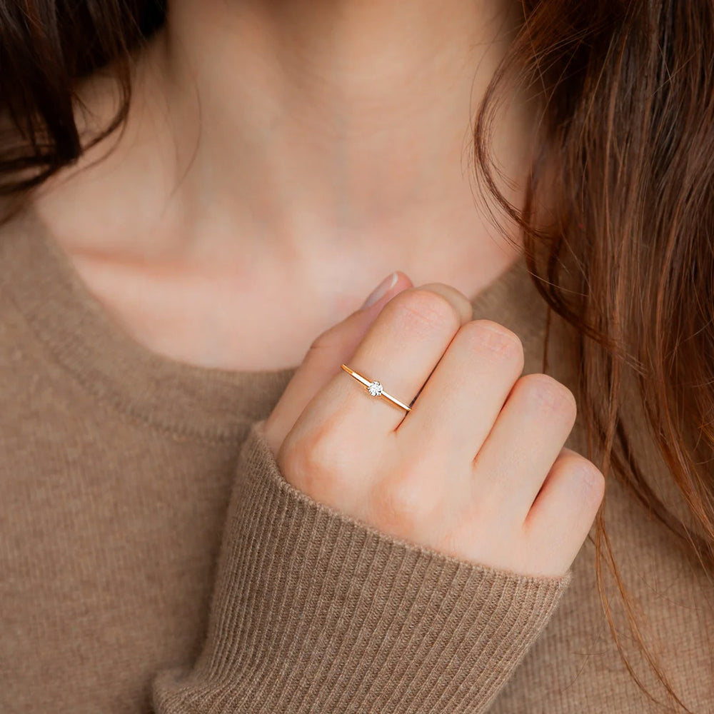 Hand wearing a gold ring on a neutral background