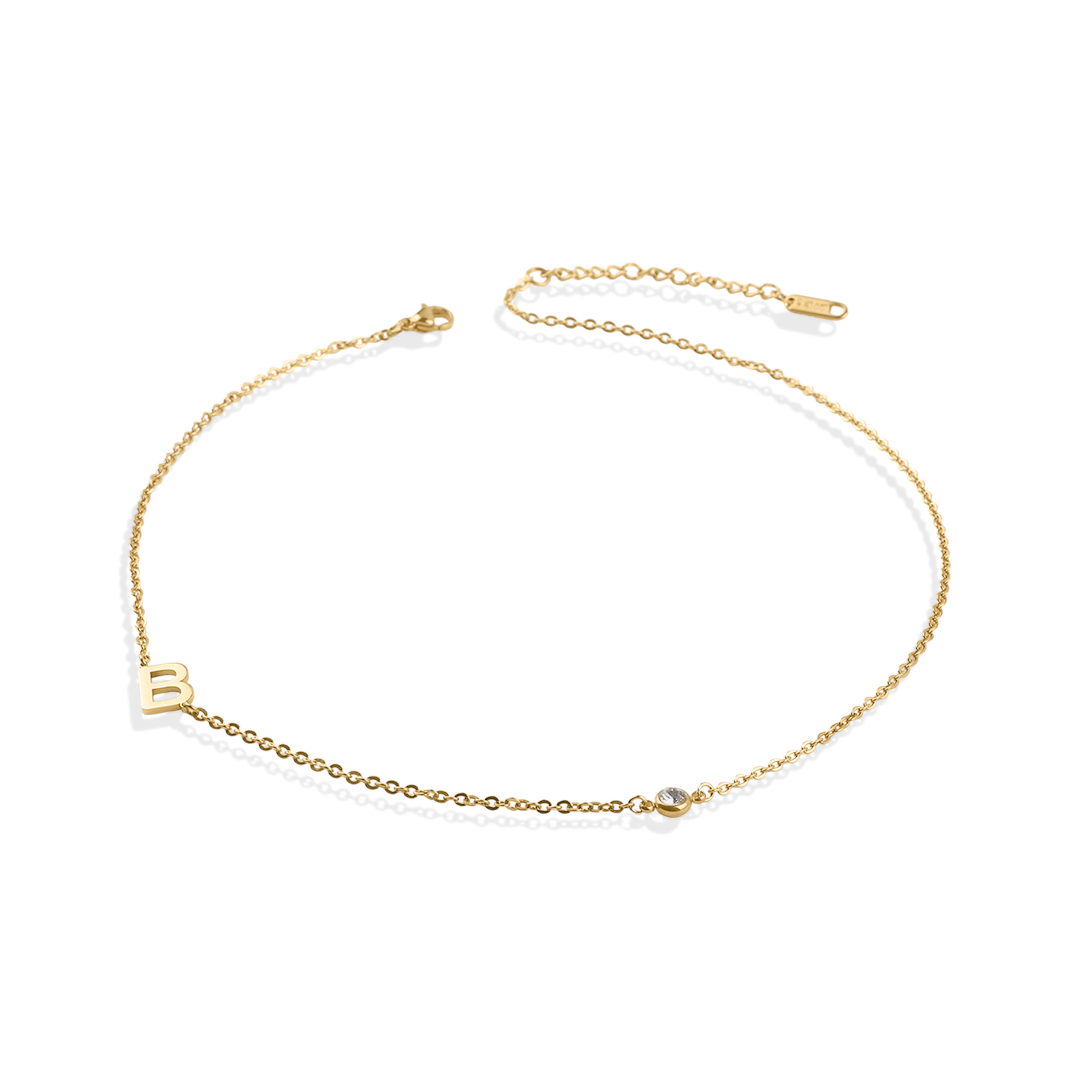 A gold initial necklace with a diamond accent, displayed against a black background.