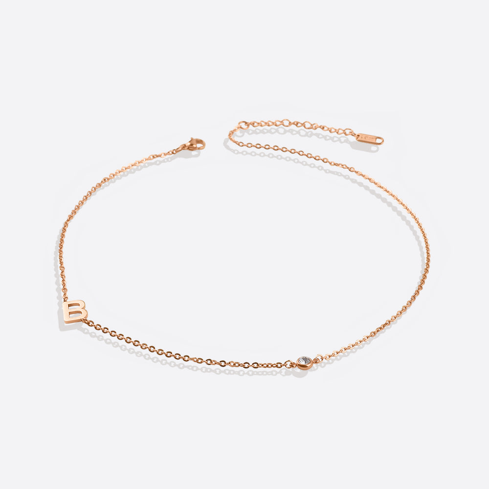A gold initial necklace with a diamond accent, displayed against a black background.