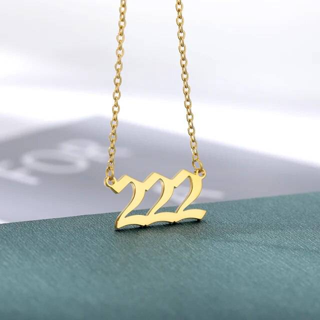 A gold-colored necklace with the angel number 444 pendant on a chain.