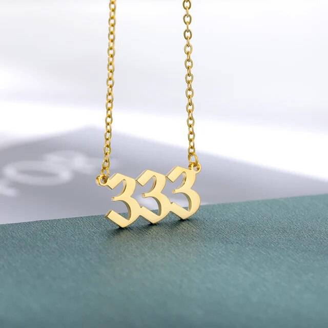 A gold-colored necklace with the angel number 444 pendant on a chain.