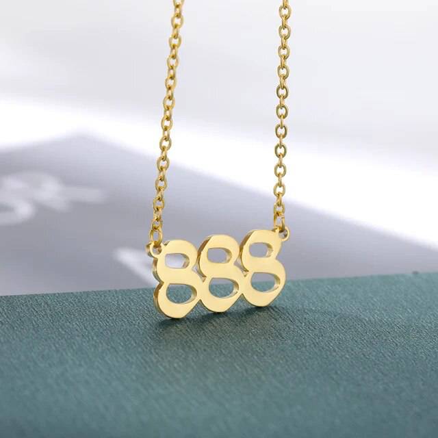 A gold-colored necklace with the angel number 444 pendant on a chain.