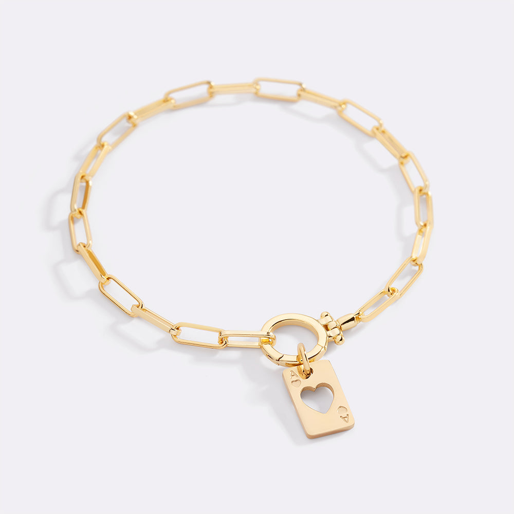 Gold bracelet with a heart-shaped tag on a light gray background