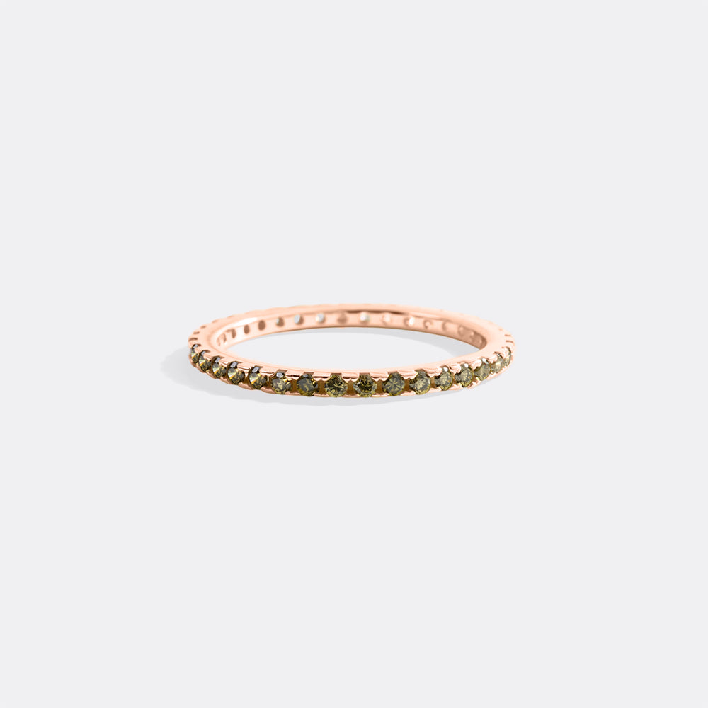 Rose gold ring with green gemstones on a light gray background