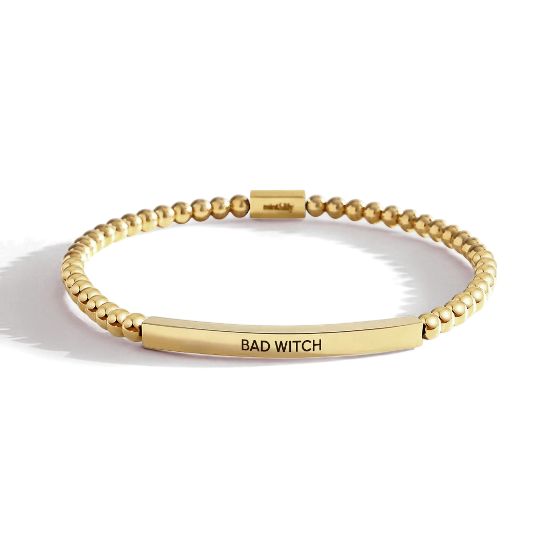 Gold bracelet with 'BAD WITCH' engraving on a light background
