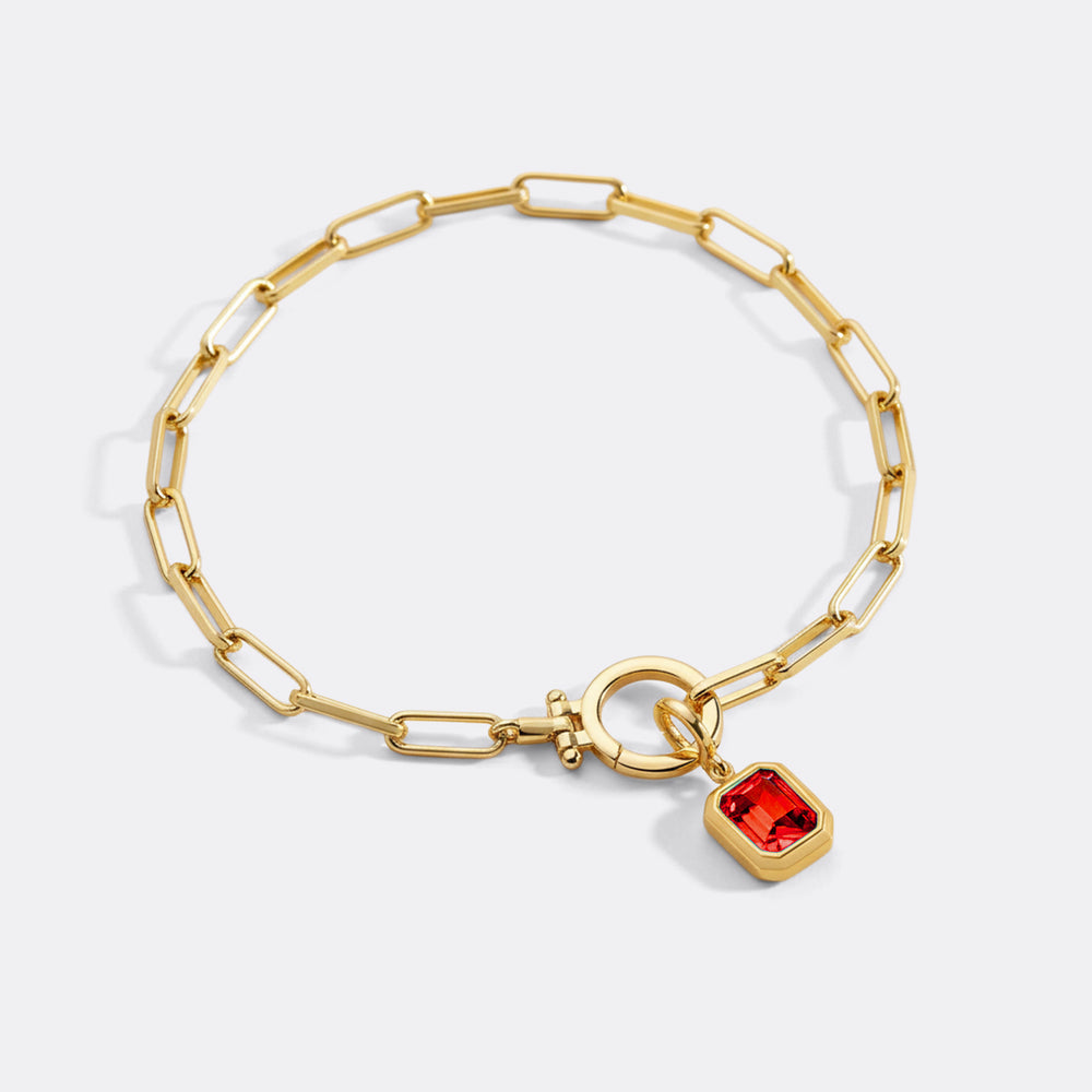 Gold bracelet with a red heart charm on a white background