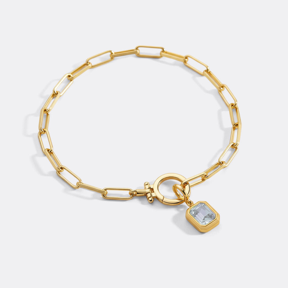 Gold bracelet with a pink gemstone charm on a white background
