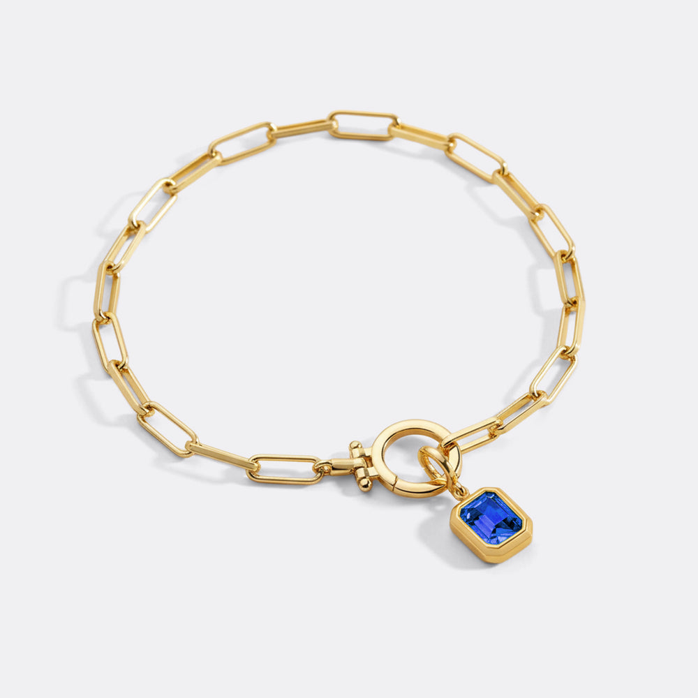 Gold bracelet with a blue gemstone charm on a white background
