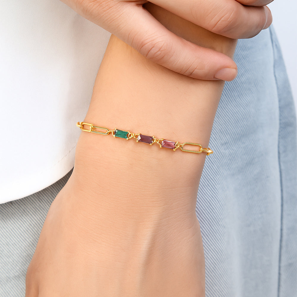 Gold bracelet with green and pink gemstones on a wrist against a light background