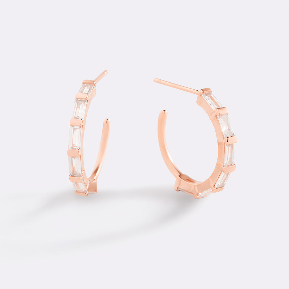 Rose gold hoop earrings with clear gemstones on a light gray background