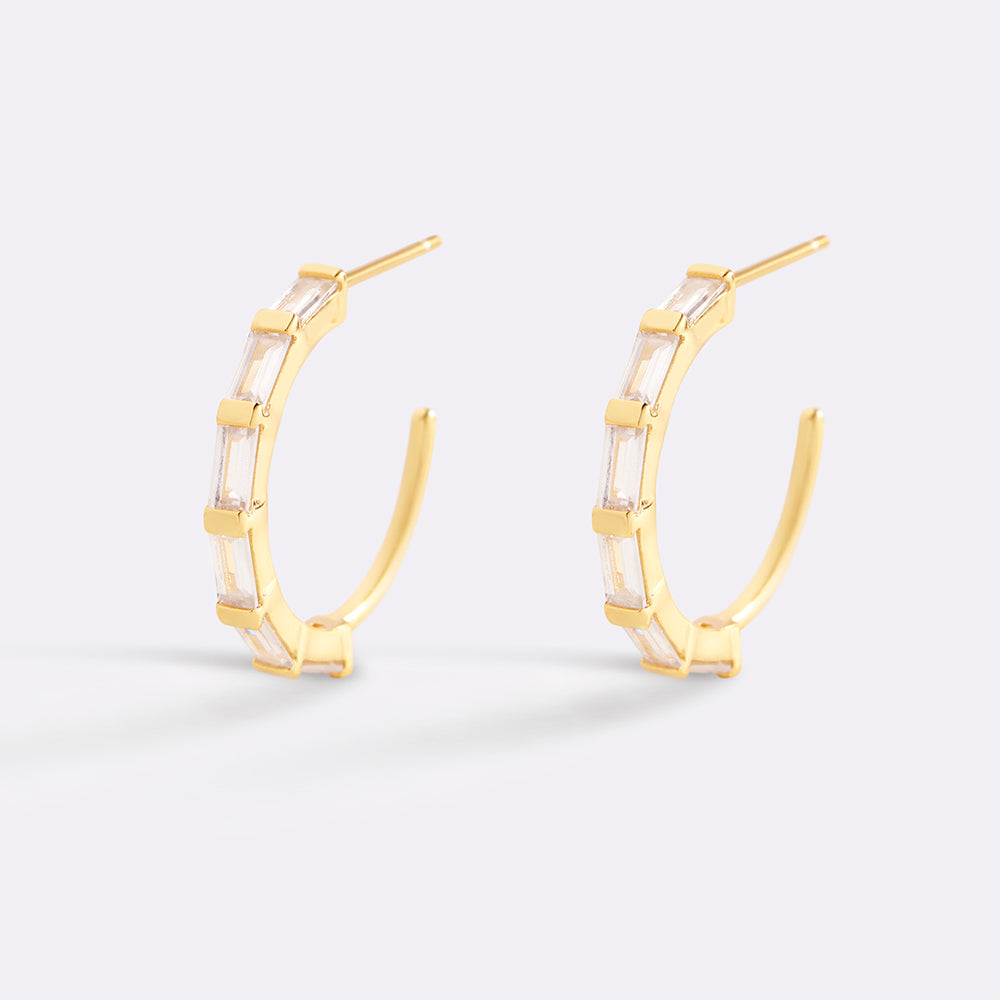 Gold hoop earrings with a white stone on a light gray background