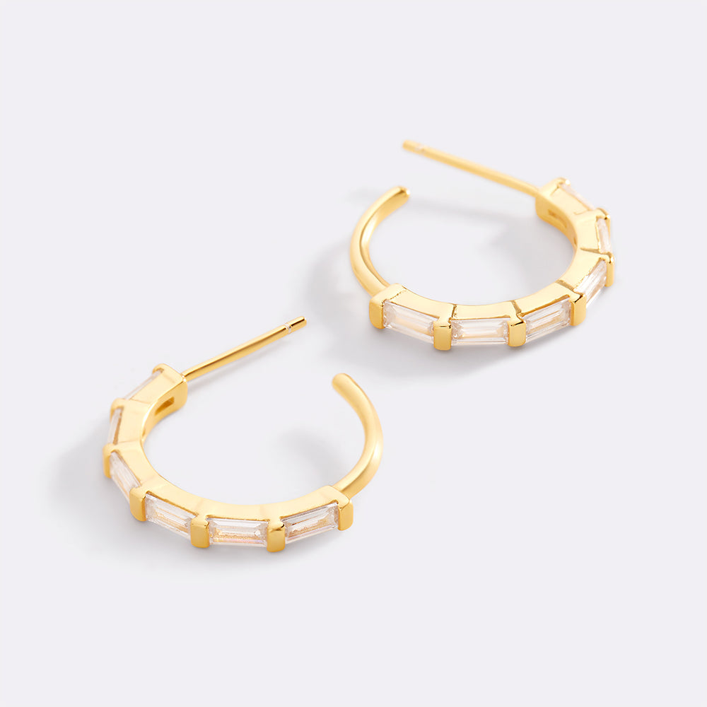 Gold hoop earrings with clear gemstones on a light gray background