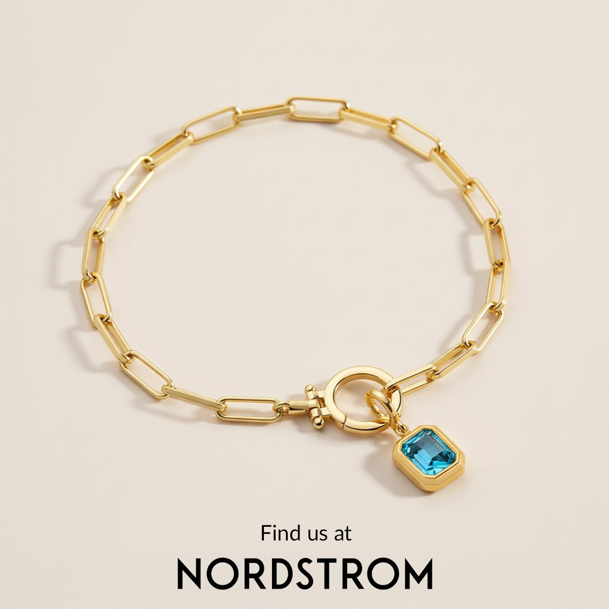 Gold chain bracelet with a blue gemstone charm on a beige background, Nordstrom branding visible.