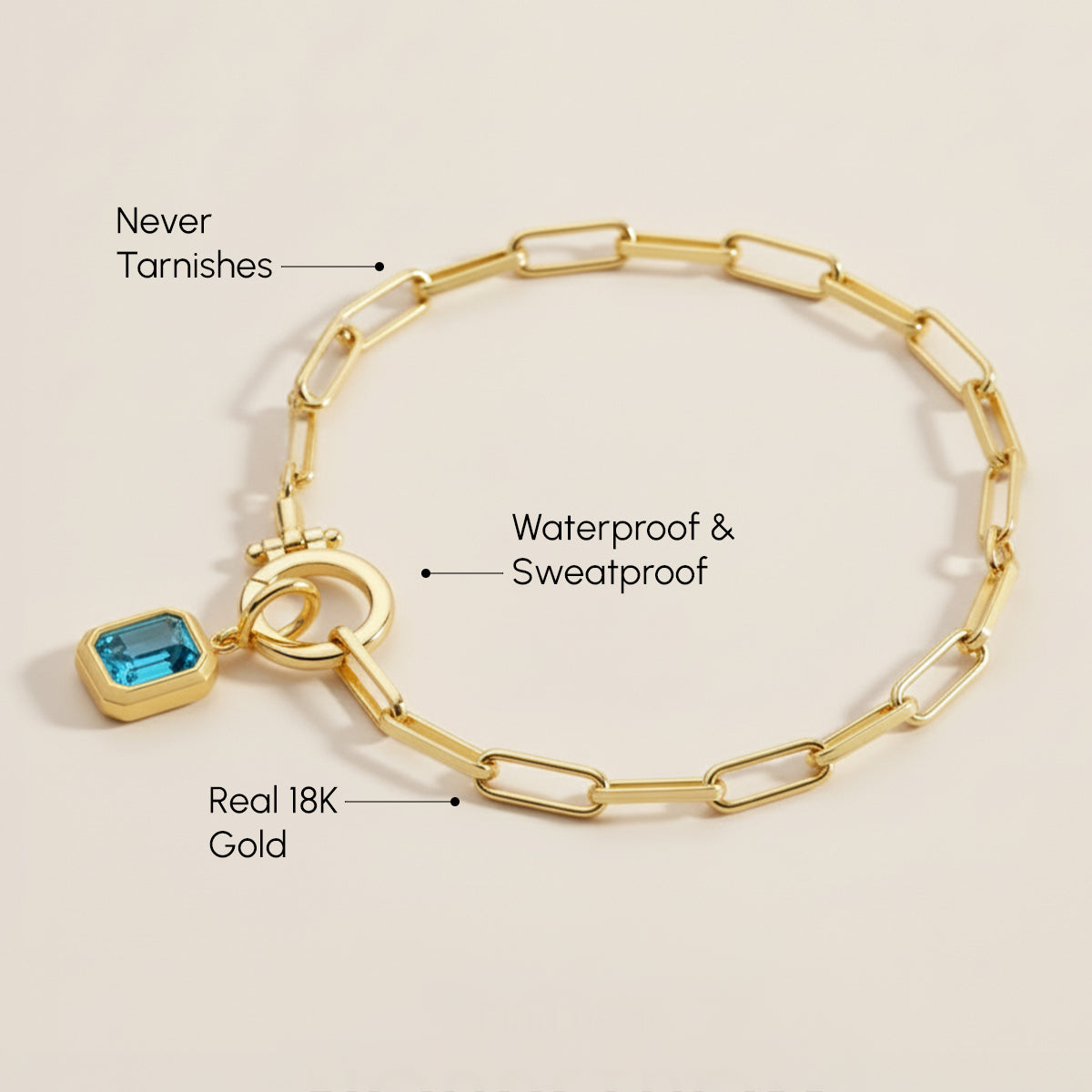 Gold bracelet with a blue gemstone charm on a beige background