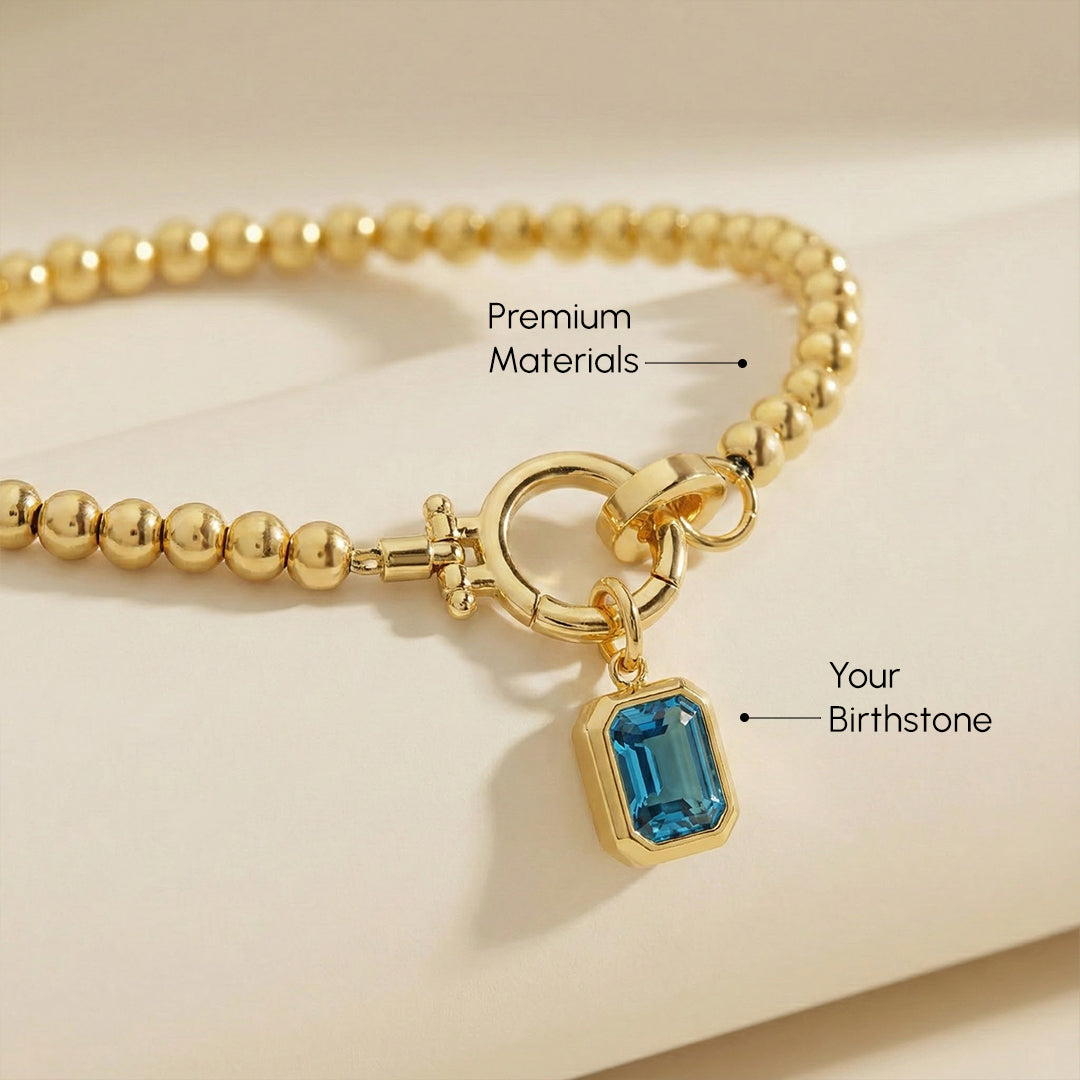 Gold bracelet with a blue gemstone charm on a beige background
