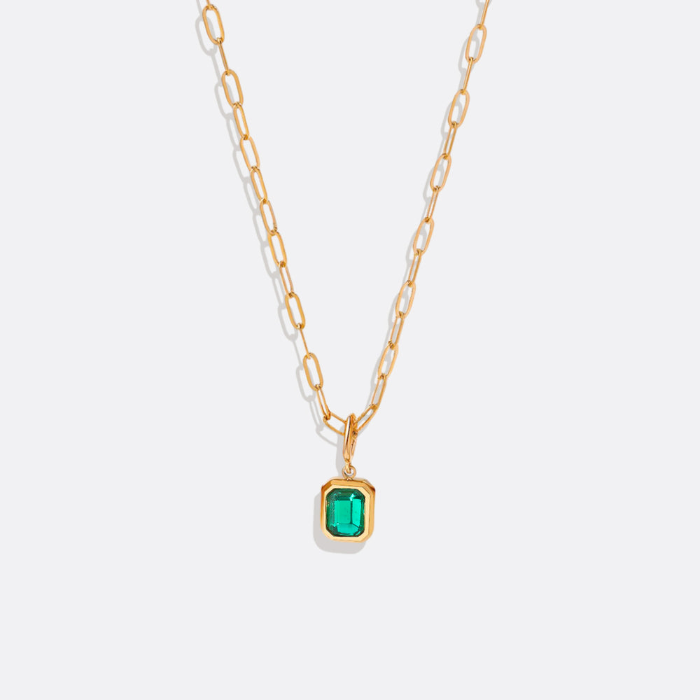 A gold-colored necklace with a baguette-cut birthstone pendant suspended from a paperclip chain.