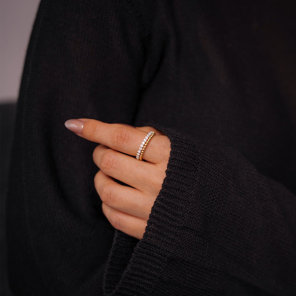Hand wearing a gold ring with a black sweater background