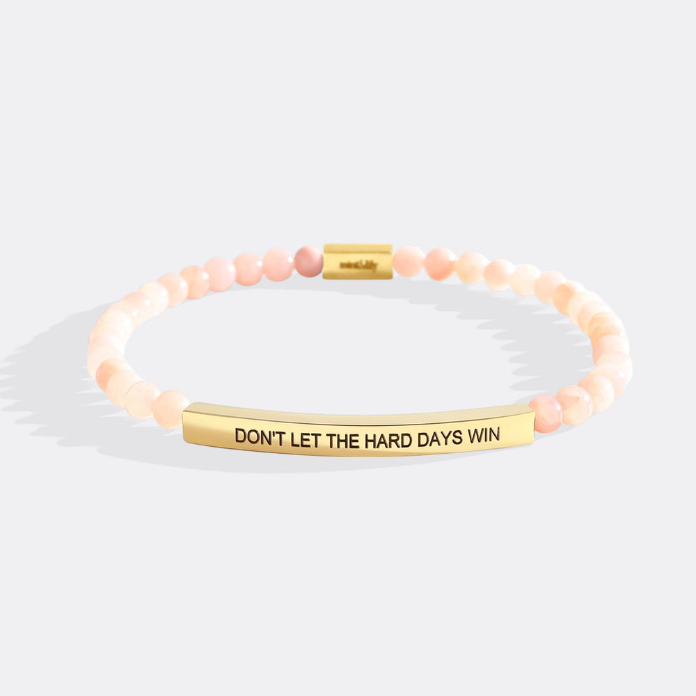Bracelet with pink beads and gold bar with motivational message on a white background