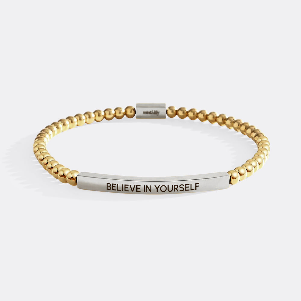 Gold beaded bracelet with a silver bar engraving 'BELIEVE IN YOURSELF' on a white background