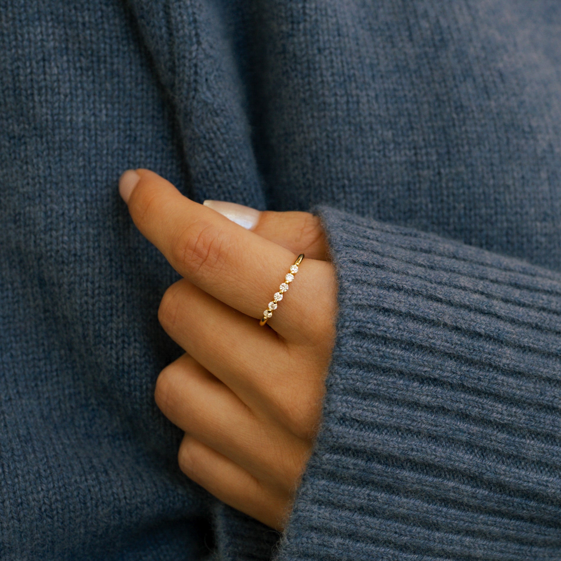 Hand wearing a diamond ring on a neutral background