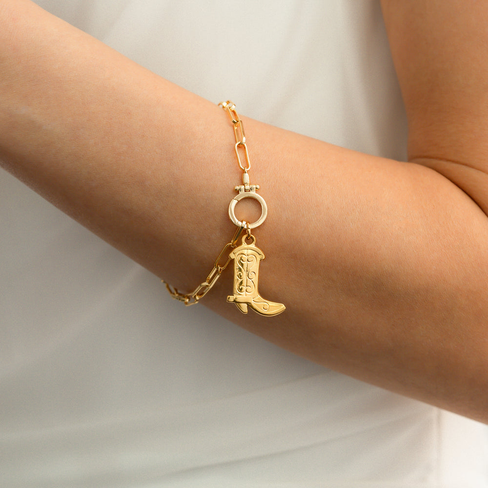 Gold bracelet with a boot charm on a person's wrist against a white background