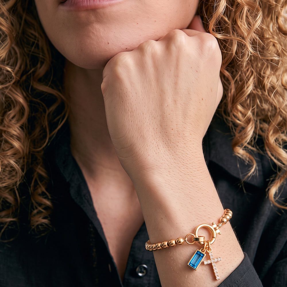 Model wearing the Cross Charm Birthstone Bracelet with December blue topaz birthstone charm on her wrist.