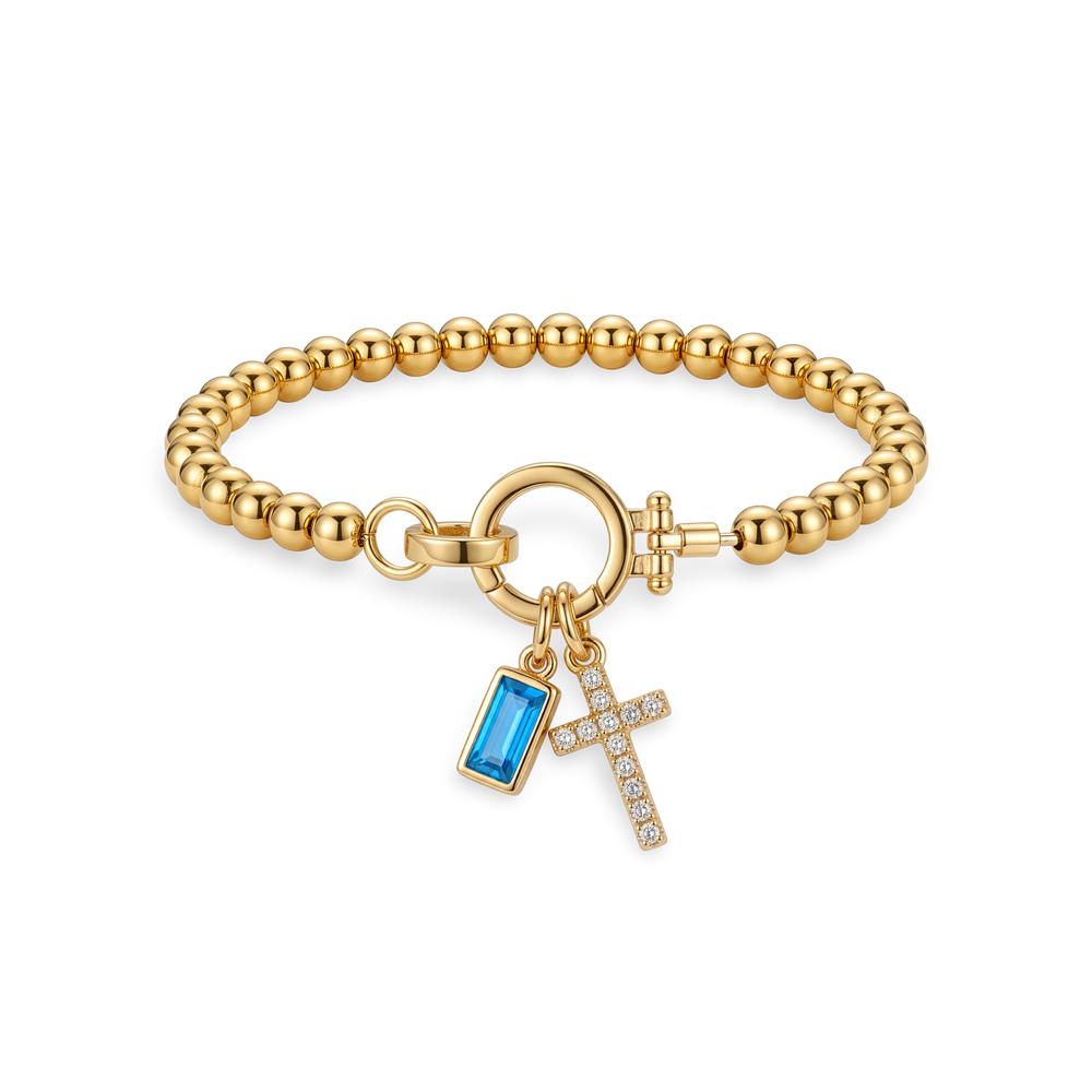 Flat lay of the Cross Charm Birthstone Bracelet with December blue topaz birthstone charm.