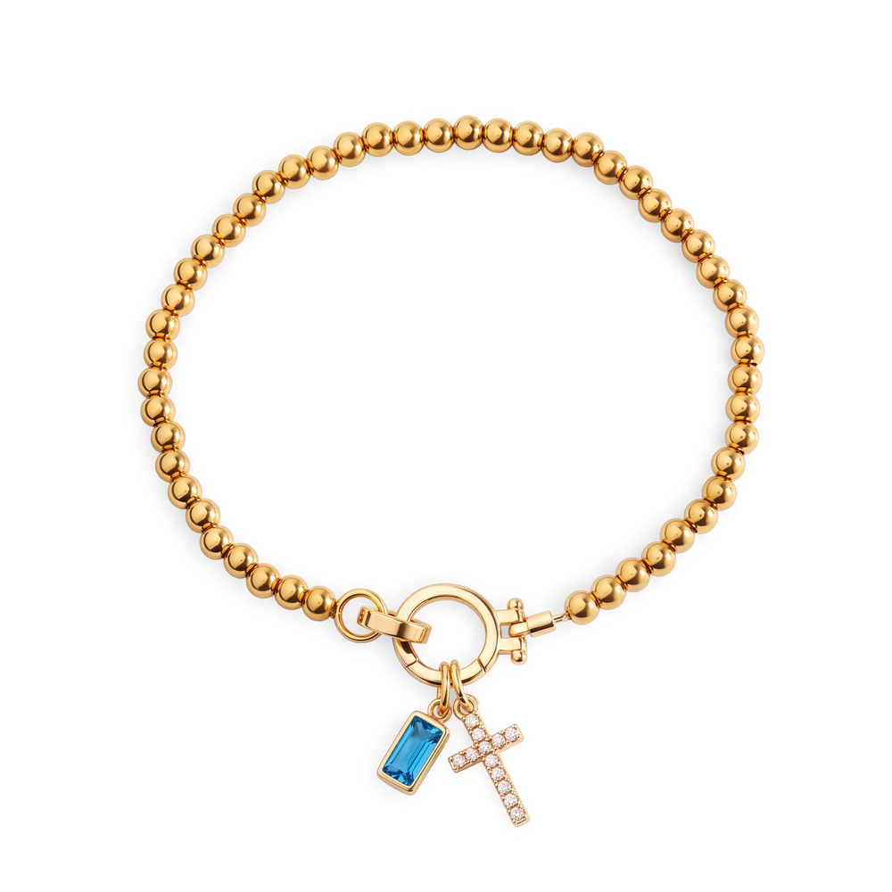Cross Charm Birthstone Bracelet with gold beaded chain, cross charm and December blue topaz birthstone charm on a white background.