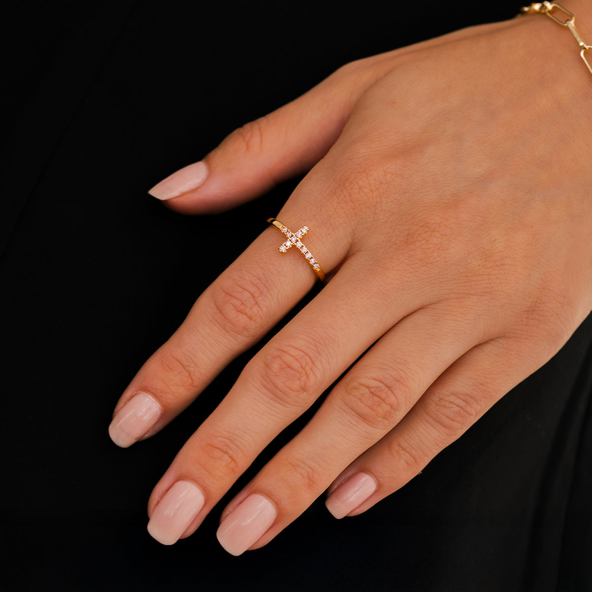 Hand wearing a gold ring with a cross design on a black background