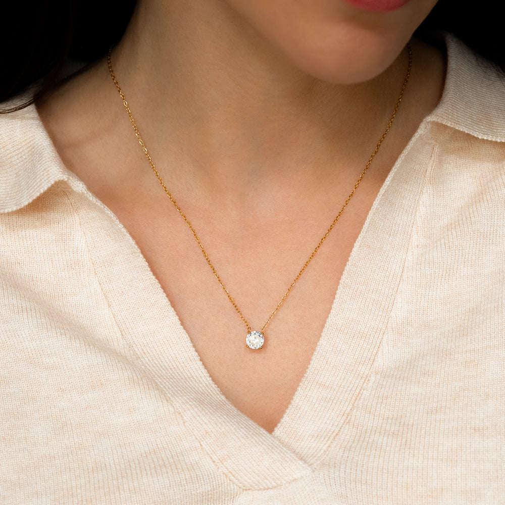 Gold necklace with a diamond pendant worn by a person in a light-colored top.
