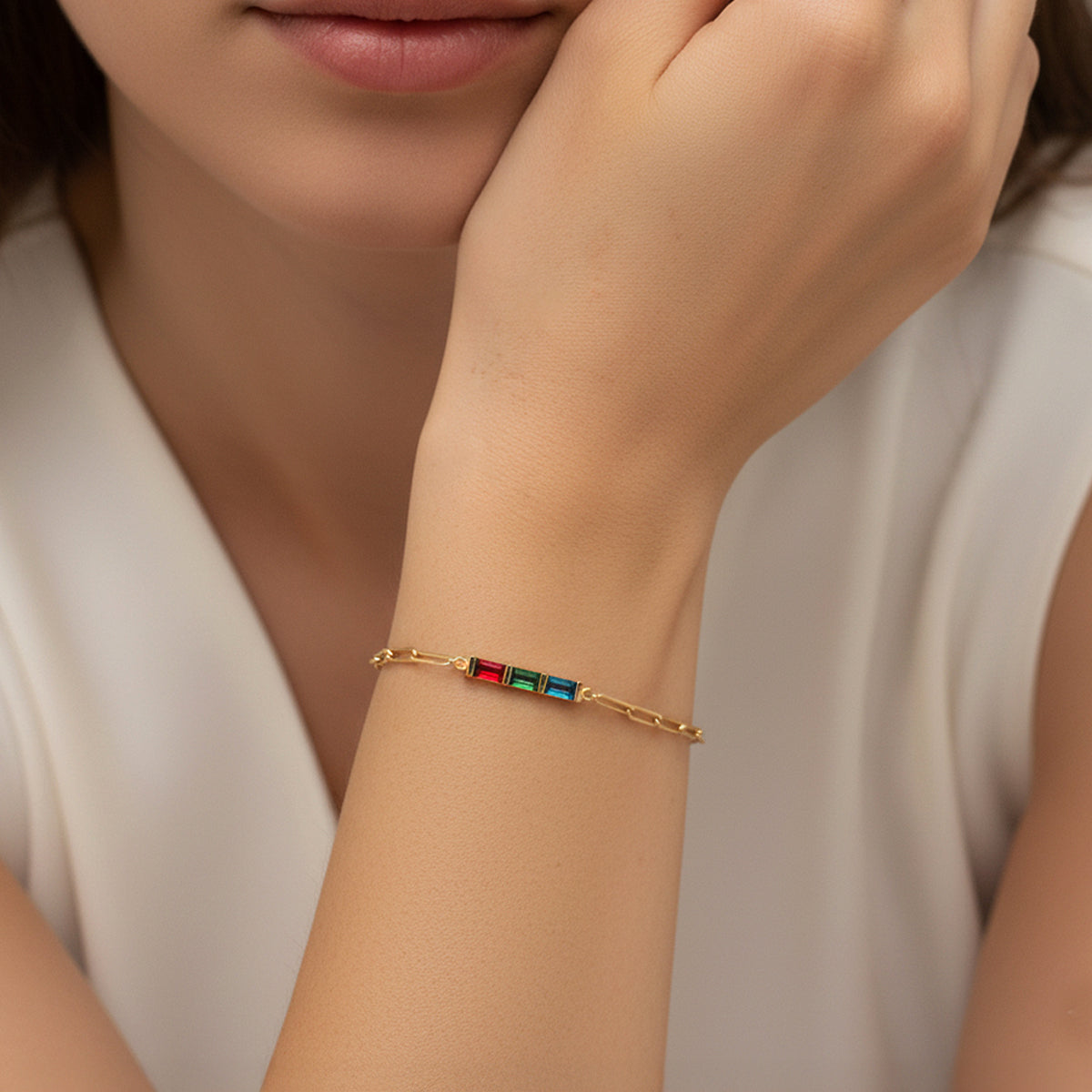 Gold bracelet with colorful gemstones on a person's wrist against a neutral background