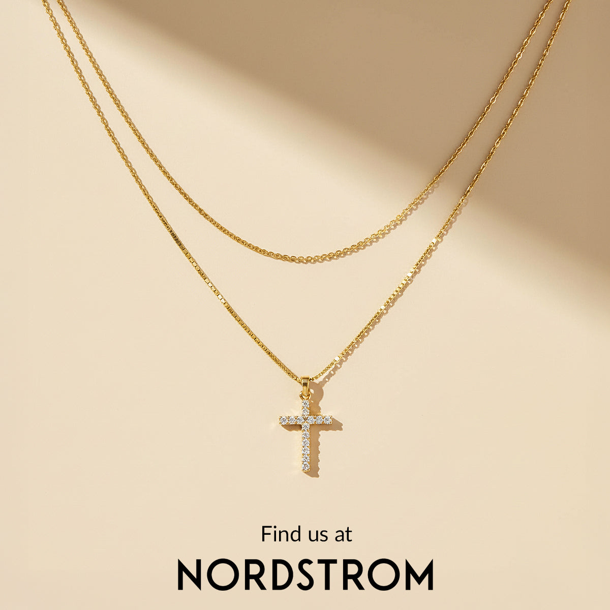 Gold necklace with a cross pendant on a beige background, featuring Nordstrom branding.