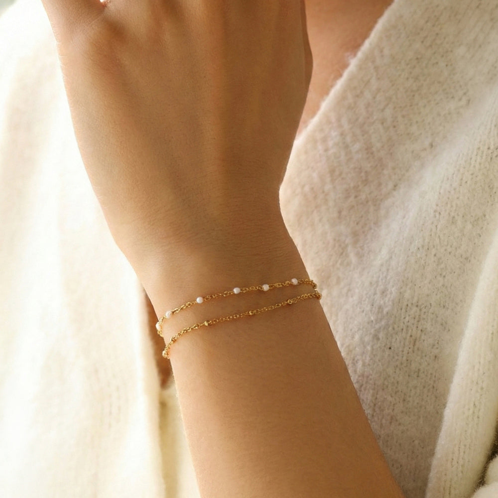 Close-up of a wrist wearing a delicate gold bracelet with small beads against a soft, neutral background.