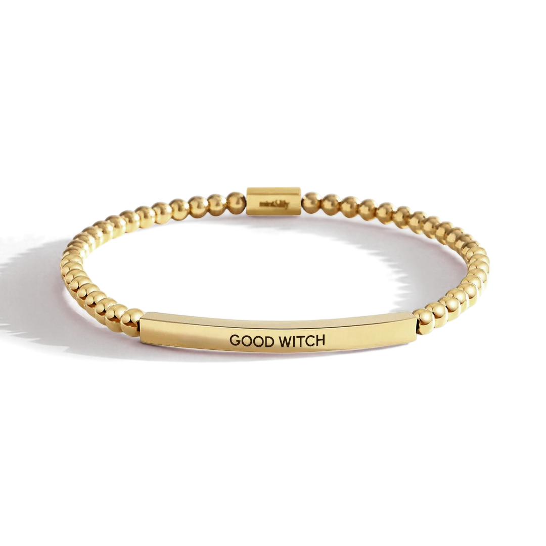 Gold bracelet with 'GOOD WITCH' engraving on a light background