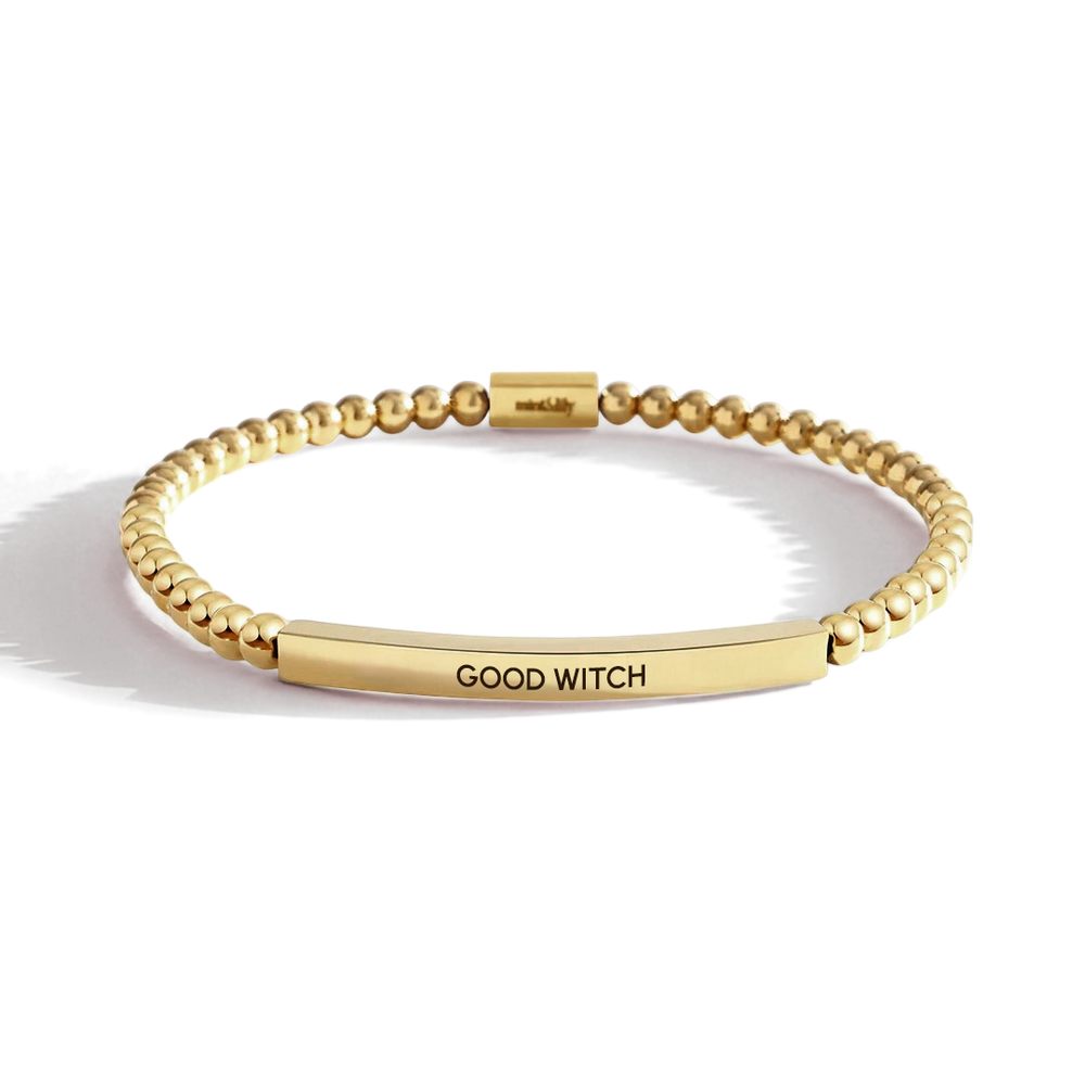 Gold bracelet with 'GOOD WITCH' engraving on a light background
