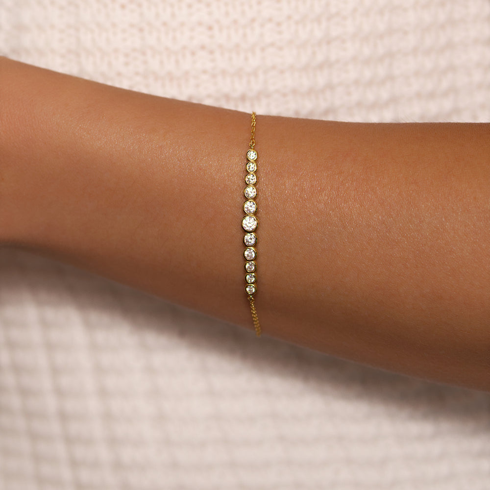 Gold bracelet with small stones on a wrist against a neutral background