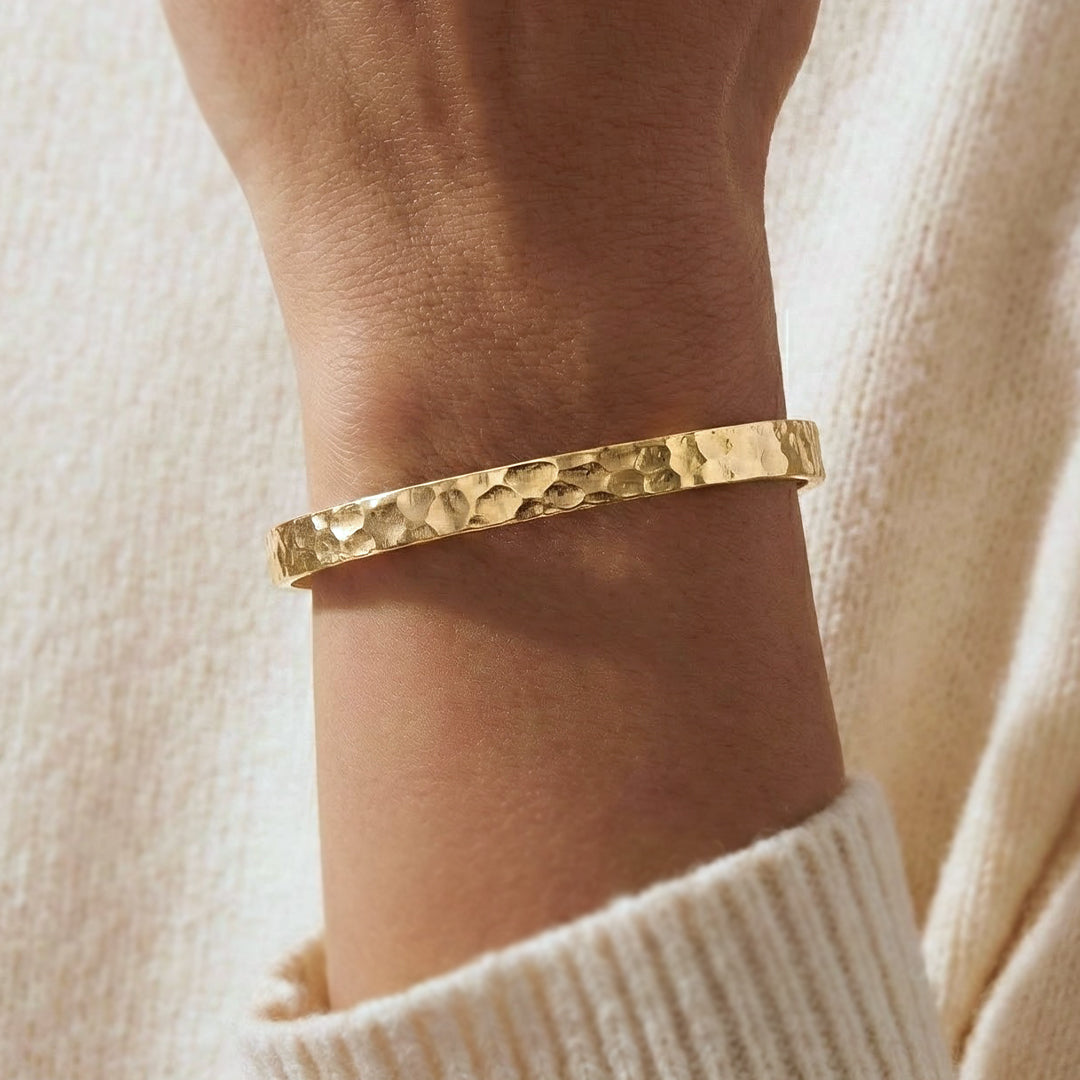 Gold bracelet on a wrist with a neutral background