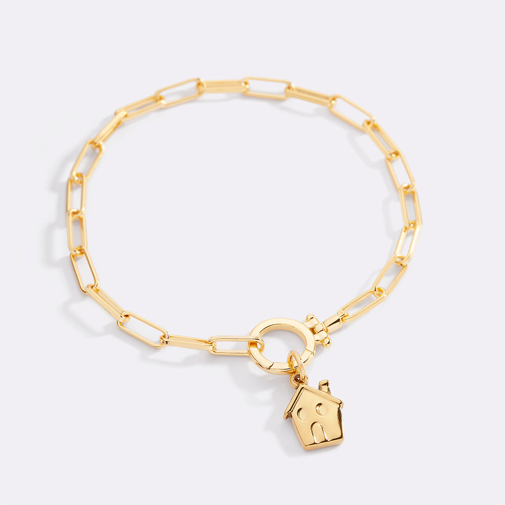 Gold bracelet with a house-shaped charm on a light gray background