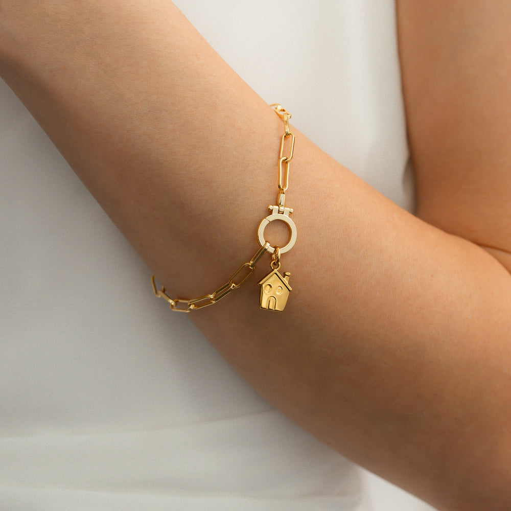 Gold bracelet with a house charm on a person's wrist against a white background