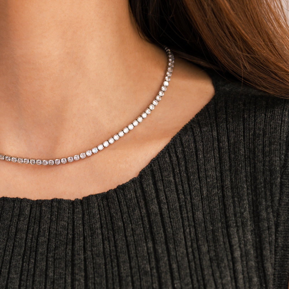 Close-up of a person wearing a delicate silver necklace against a dark gray sweater.