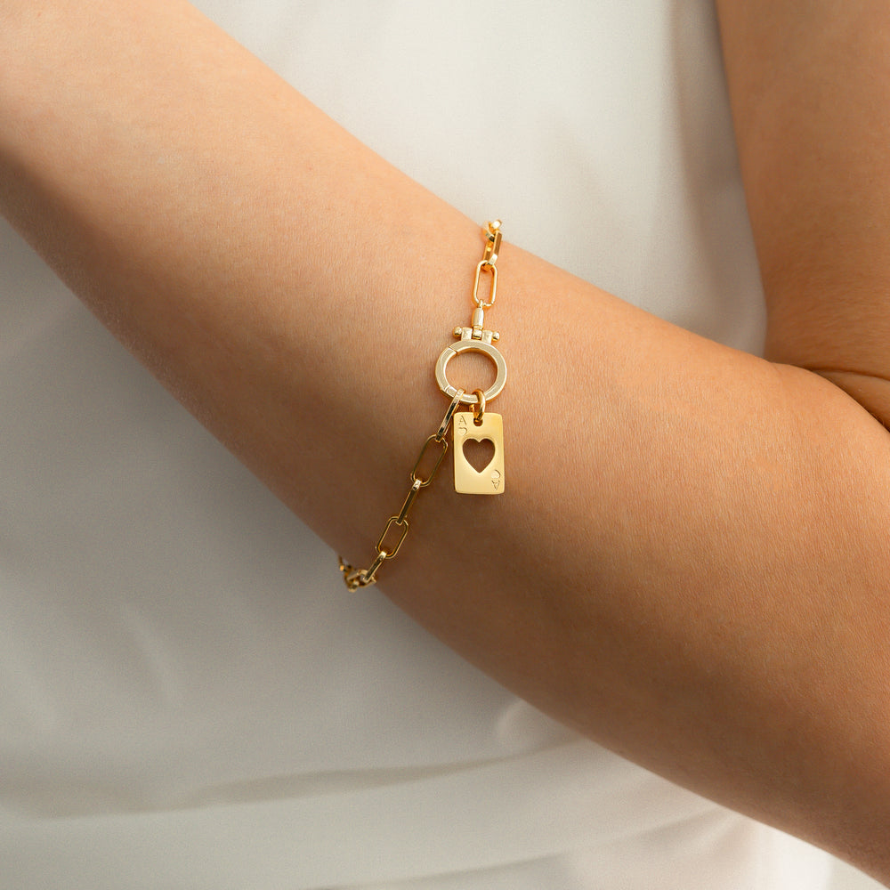 Gold bracelet with heart charm on a person's wrist against a white background