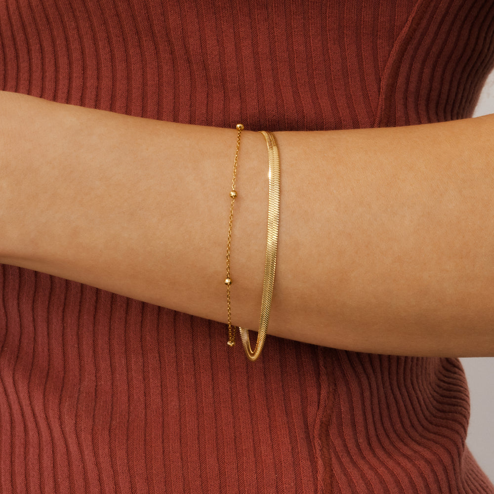 Gold bracelet on a person's wrist against a red ribbed sweater background